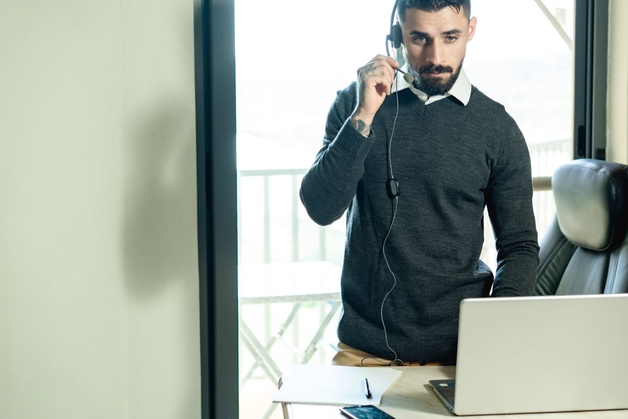 A man in an office with a headset providing customer service from a laptop.